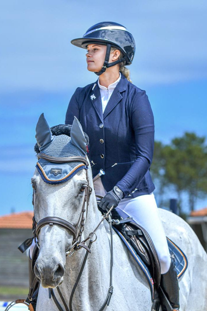 Woman in equestrian attire riding a white horse in an outdoor setting